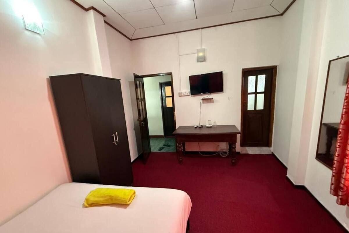 Quarto de hotel com cama, escrivaninha, televisão e armário.