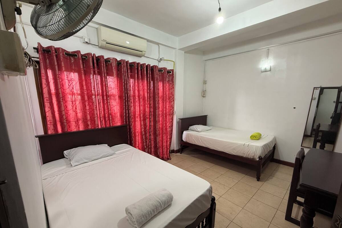 Quarto com duas camas de solteiro, um ventilador, ar condicionado, um espelho e uma mesinha.