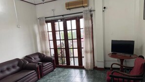 A living room with a sofa, a television on a stand, a small table, and a view through a glass door. - Airport Residencies (Katunayake)