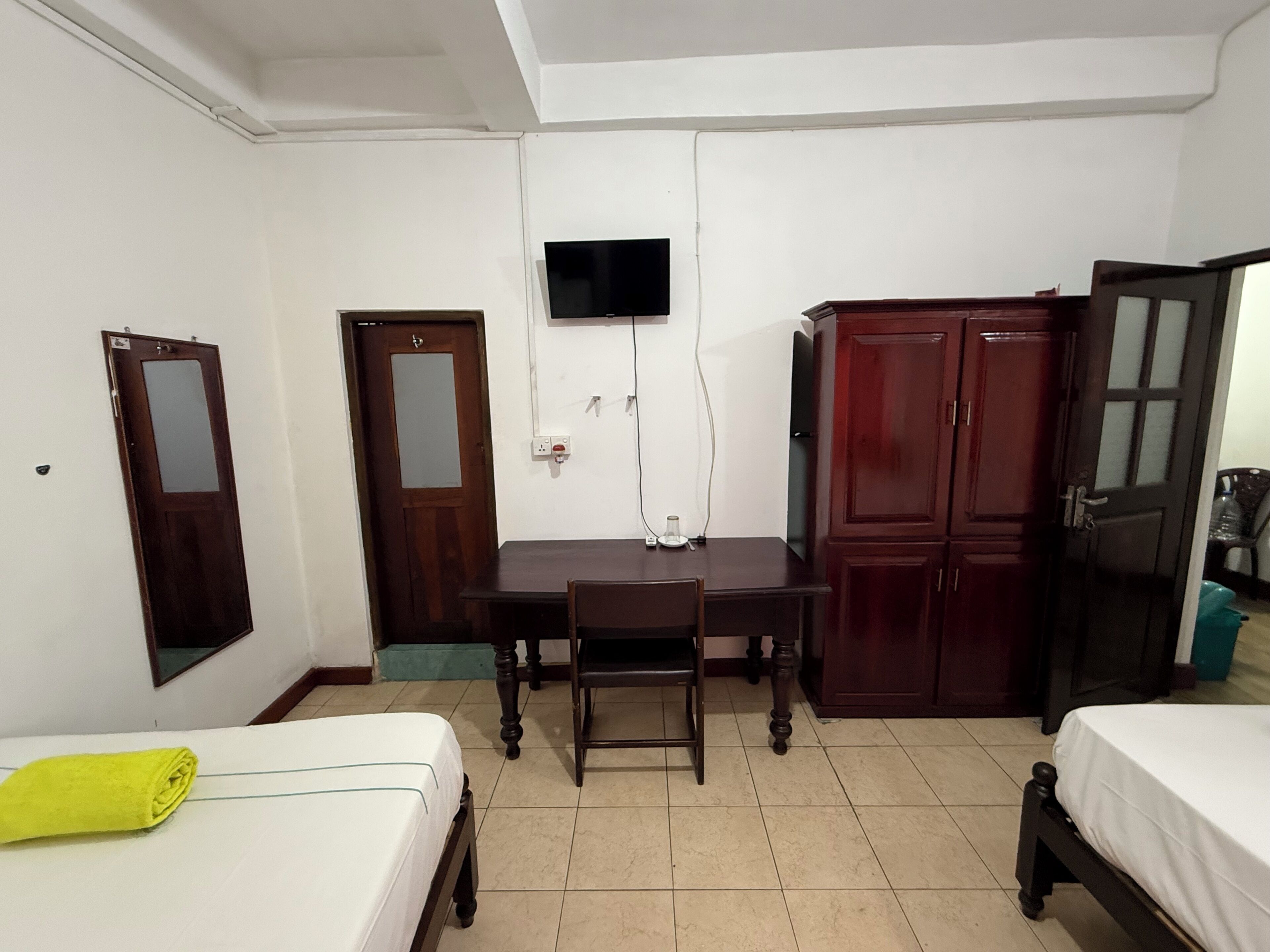 A room with a bed, a desk, a chair, a TV mounted on the wall, and a wardrobe.