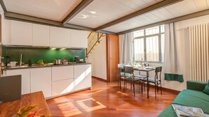 A modern kitchen with white cabinets, a dining area with a table and chairs, and a green sofa. - Elegant Loft in Citylife Wifi - A/C - (Milan)