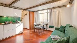 A modern kitchen with wooden flooring, a dining area with a table and chairs, and a green sofa. - Elegant Loft in Citylife Wifi - A/C - (Milan)
