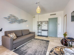 Ein modernes Wohnzimmer mit einem grauen Sofa, einem schwarz-weißen Teppich, einer wandmontierten Leuchte und einem dekorativen Wandbild mit Fischen.