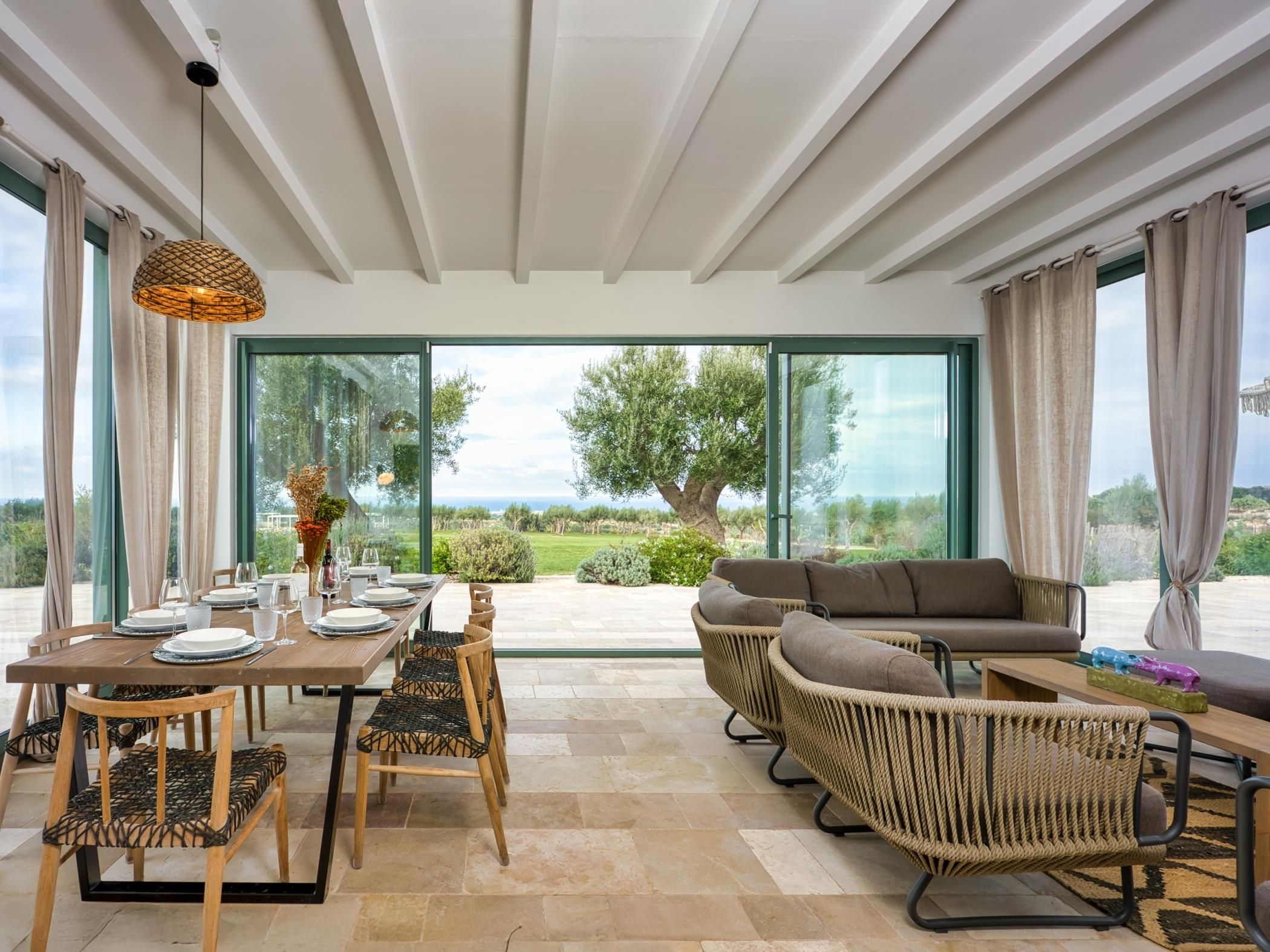 A dining area with a table set for four, surrounded by wicker chairs, and a sofa with cushions.