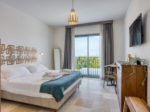 Ein Schlafzimmer mit Bett, Schreibtisch, Stuhl, Fernseher und einem Balkon mit Blick.