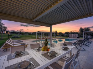 Ein Essbereich im Freien mit Pool, Liegestühlen und Blick auf einen Sonnenuntergang.