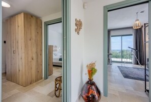 Ein modernes Interieur mit einem Holzschrank, einer Vase mit Trockenblumen und Blick durch eine Glastür auf einen Balkon.