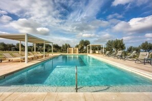 Ein rechteckiger Swimmingpool mit klarem, blauem Wasser, umgeben von Liegestühlen und überdachten Sitzbereichen.