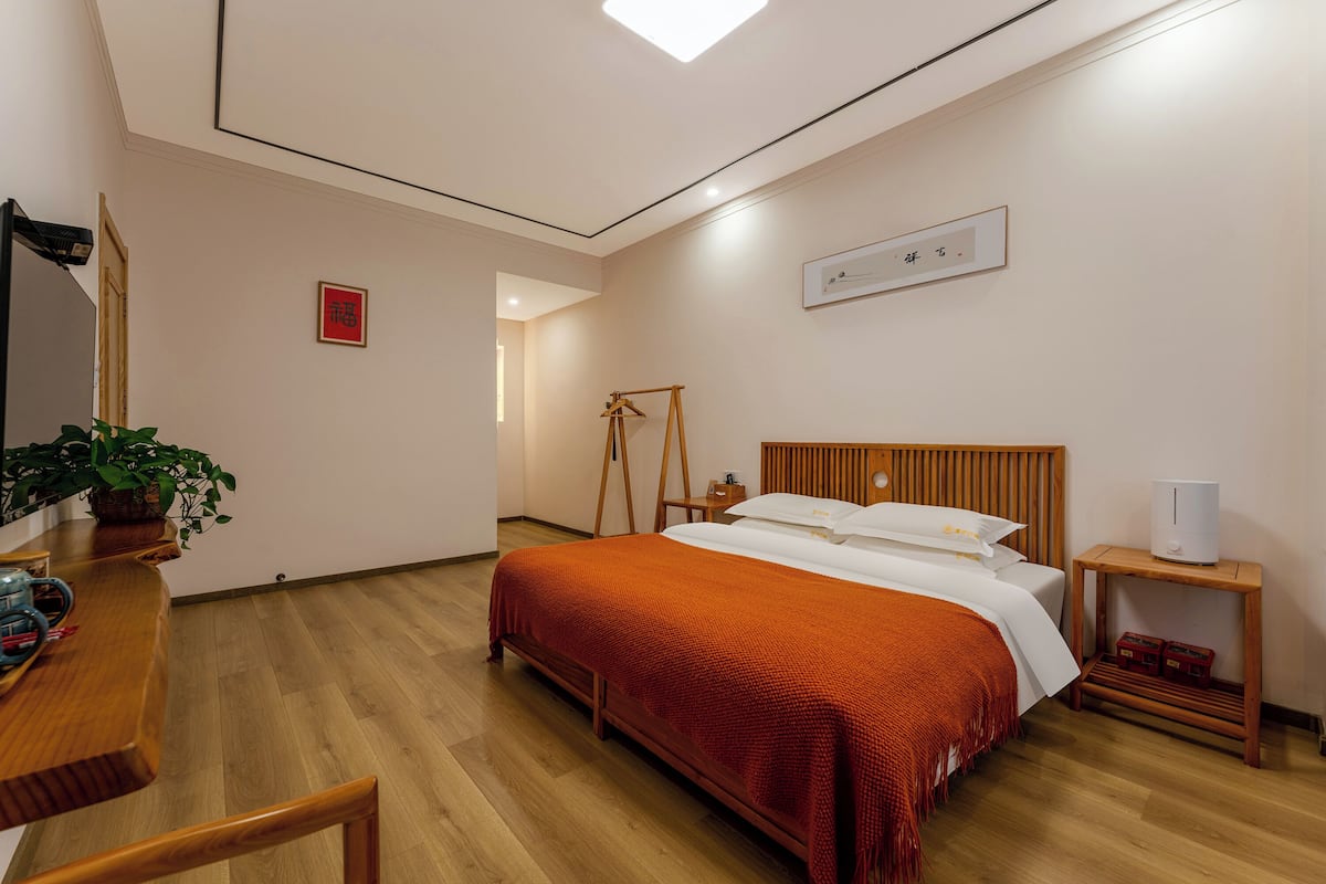 A bedroom with a wooden bed, a bedside table, a hanging light, a small plant, and a red sign on the wall.