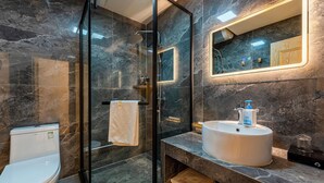 A bathroom with a glass-enclosed shower, a white toilet, a sink with a mirror, and marble walls. - ManBuYunDuan.Theme Inn (Xinzhou)