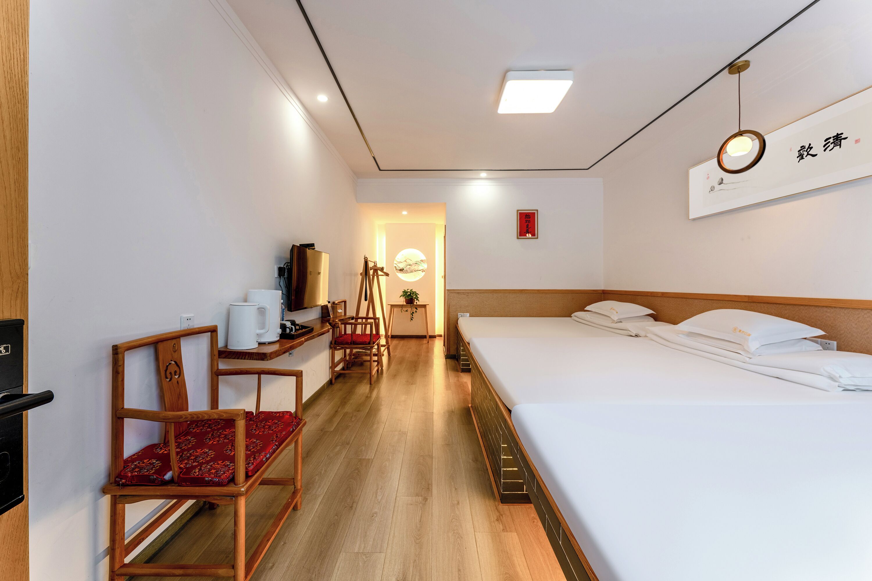 Habitación de hotel con cama, escritorio y silla, una mesita con planta y un cartel en la pared.