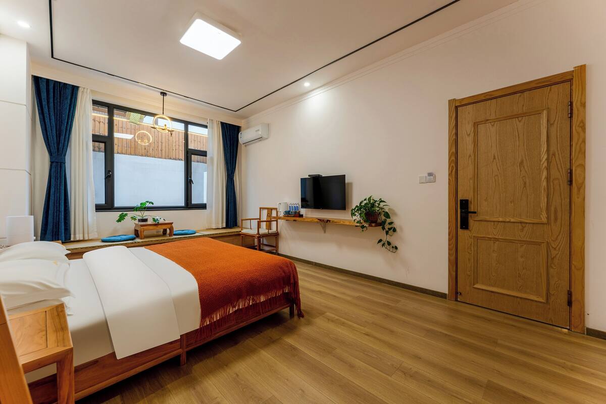 A hotel room with a bed, a TV, a wooden door, and a window with curtains.