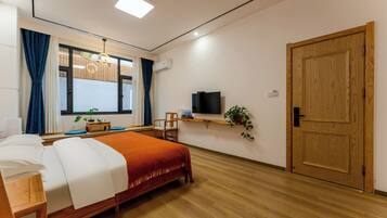 Una habitación de hotel con una cama, un televisor, una puerta de madera y un ventanal con cortinas.