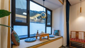 A room with a large window, a wooden bench with cushions, a small table with a vase and teapot, and a wooden chair with a red cushion. - ManBuYunDuan.Theme Inn (Xinzhou)