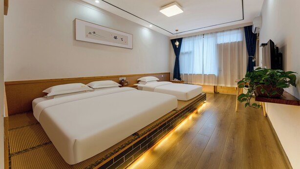 A hotel room with a large bed, bedside tables, a small desk, a potted plant, and a window with curtains. - ManBuYunDuan.Theme Inn (Xinzhou)