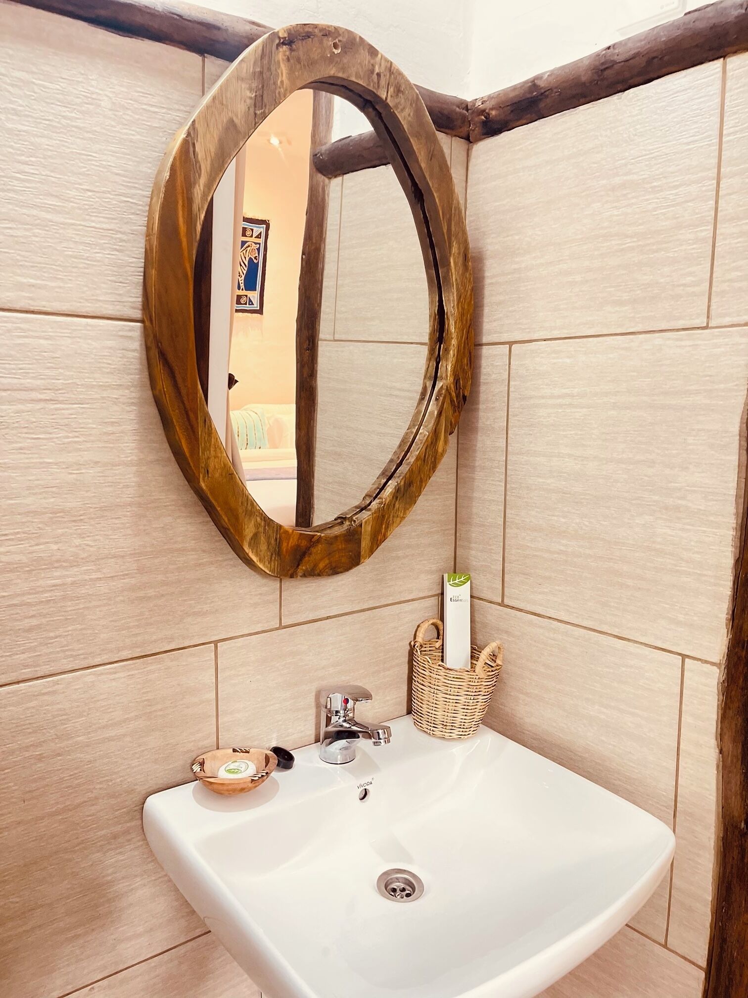 Un baño con espejo de marco de madera, lavamanos blanco y una cesta de mimbre con artículos de aseo.