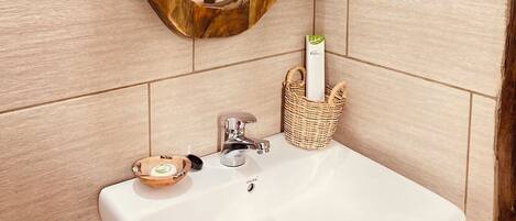 Un baño con espejo de marco de madera, lavamanos blanco y una cesta de mimbre con artículos de aseo.