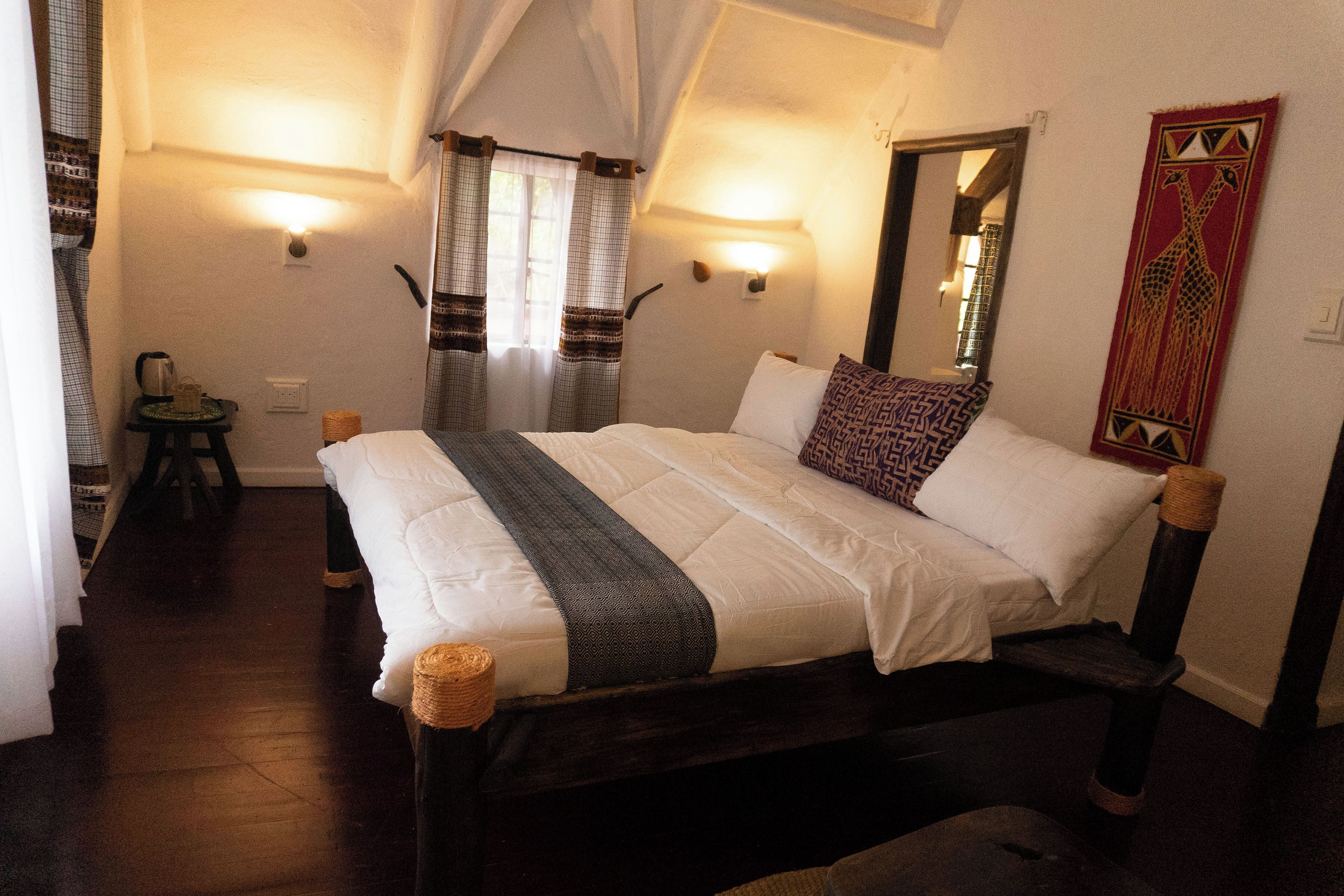 A bedroom with a bed, bedside lamps, a mirror, and a wall-mounted tapestry.