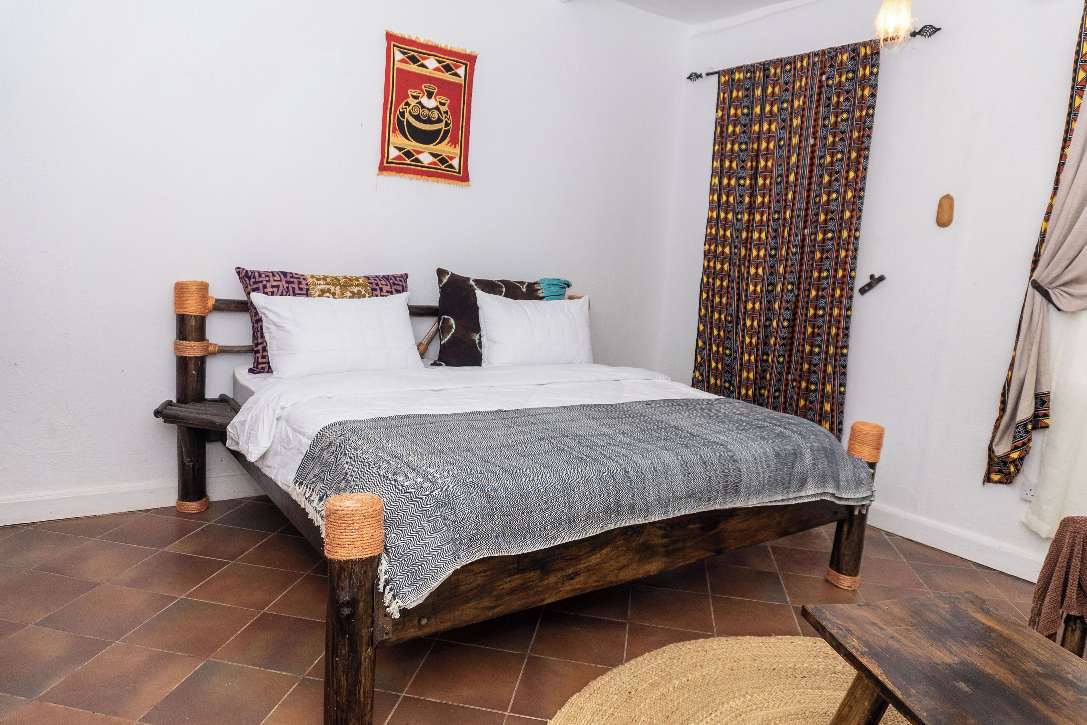 A bed with a patterned blanket, a wall tapestry, and a patterned curtain.