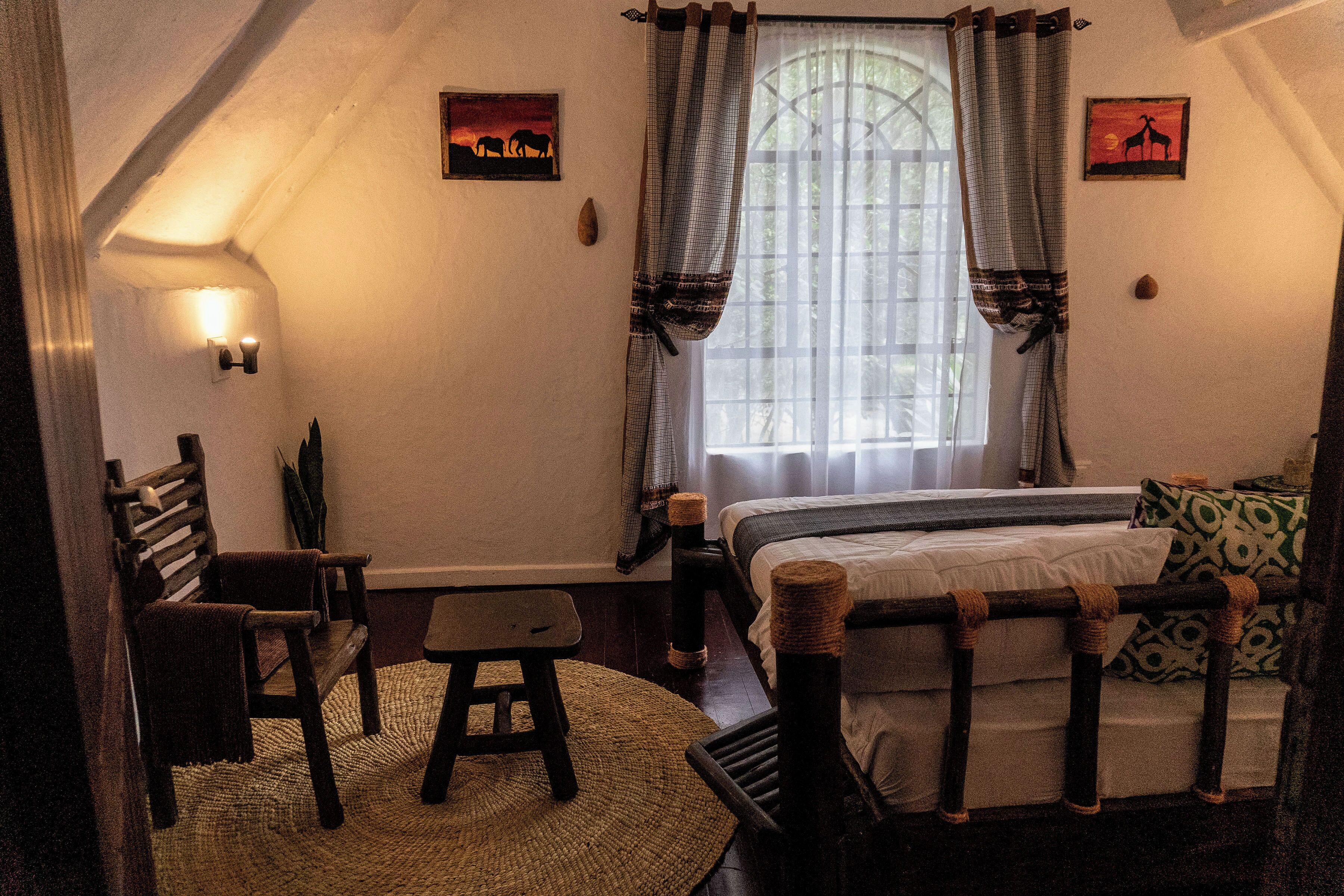 A cozy bedroom with a bed, a chair, a small stool, a woven rug, and two wall-mounted picture frames.