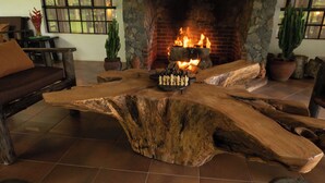 A rustic wooden coffee table with a chess set in front of a fireplace.