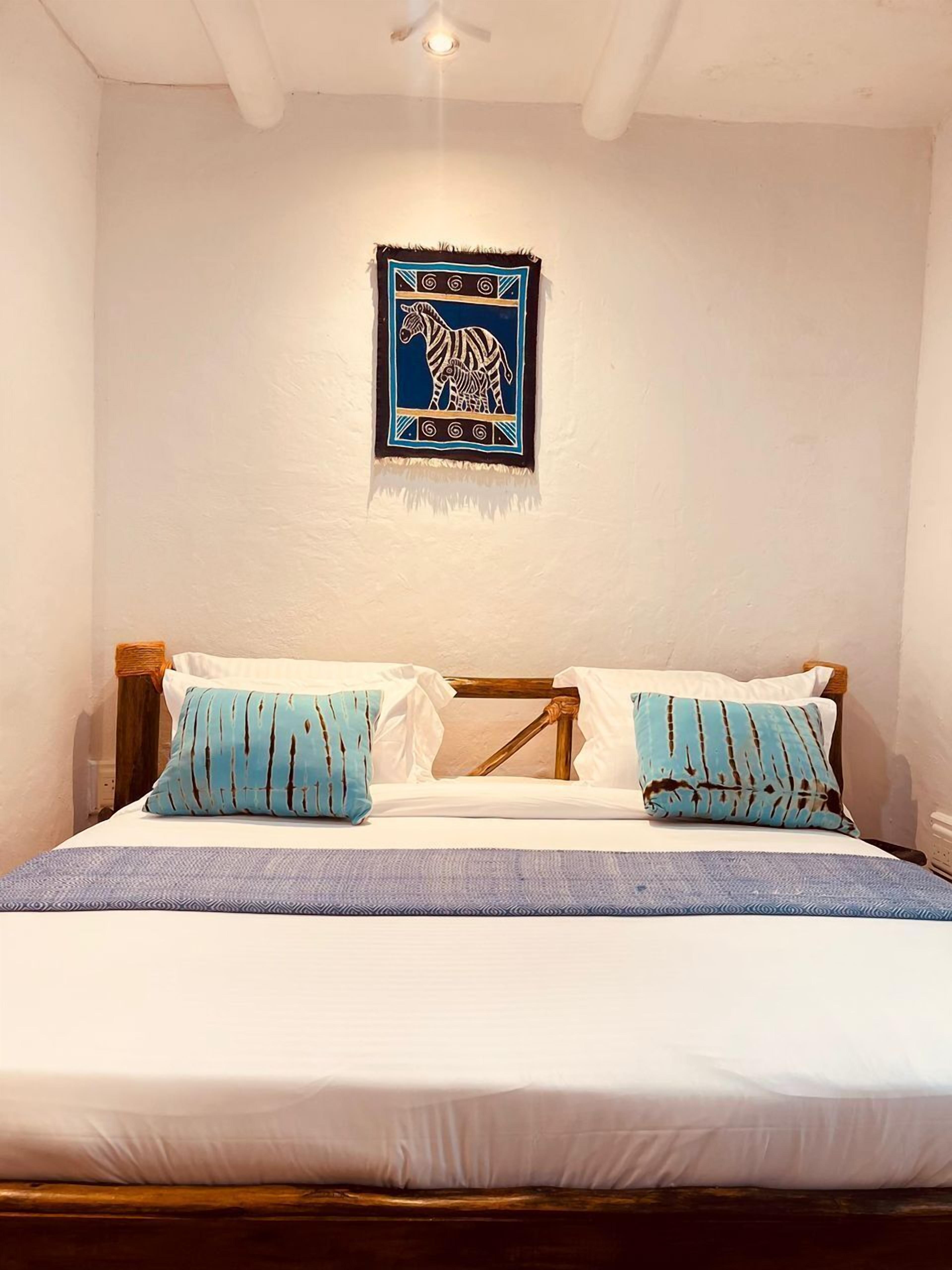 A bedroom with a bed, two pillows, a blue and white blanket, and a wall hanging of a zebra.