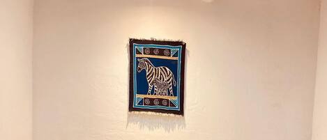 A bedroom with a bed, two pillows, a blue and white blanket, and a wall hanging of a zebra.