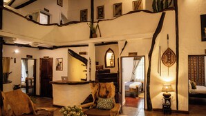 A spacious lobby with a reception desk, wooden furniture, a staircase, and a bed in the background.