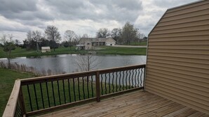 A wooden deck with a metal railing, overlooking a body of water and houses in the background. - Superb 3-bedroom condo in Wellman within walking distance from two playgrounds. (Wellman)