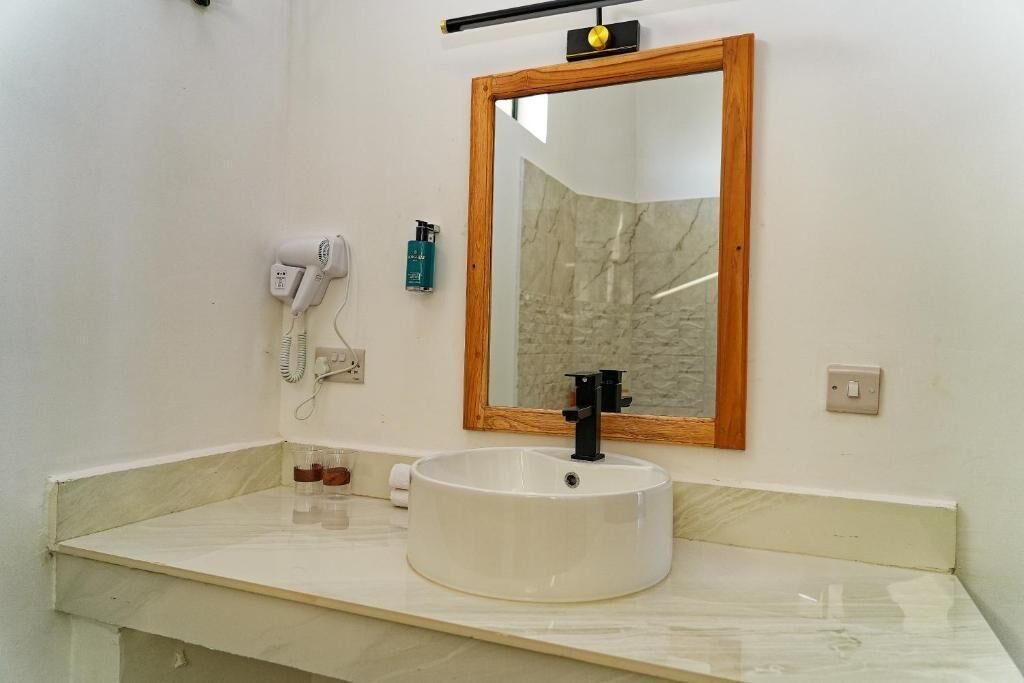 A bathroom with a white sink, a mirror with a wooden frame, a hairdryer, and a bottle of shampoo.