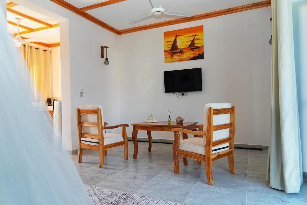 A room with a ceiling fan, a TV mounted on the wall, wooden chairs, a small table, and a painting of sailboats.