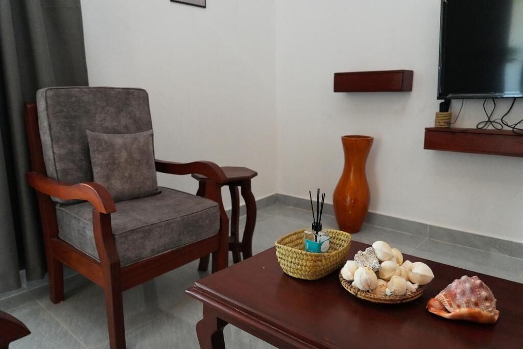 A living room with a wooden chair, a small table with a basket of items, a vase, and a television on the wall.