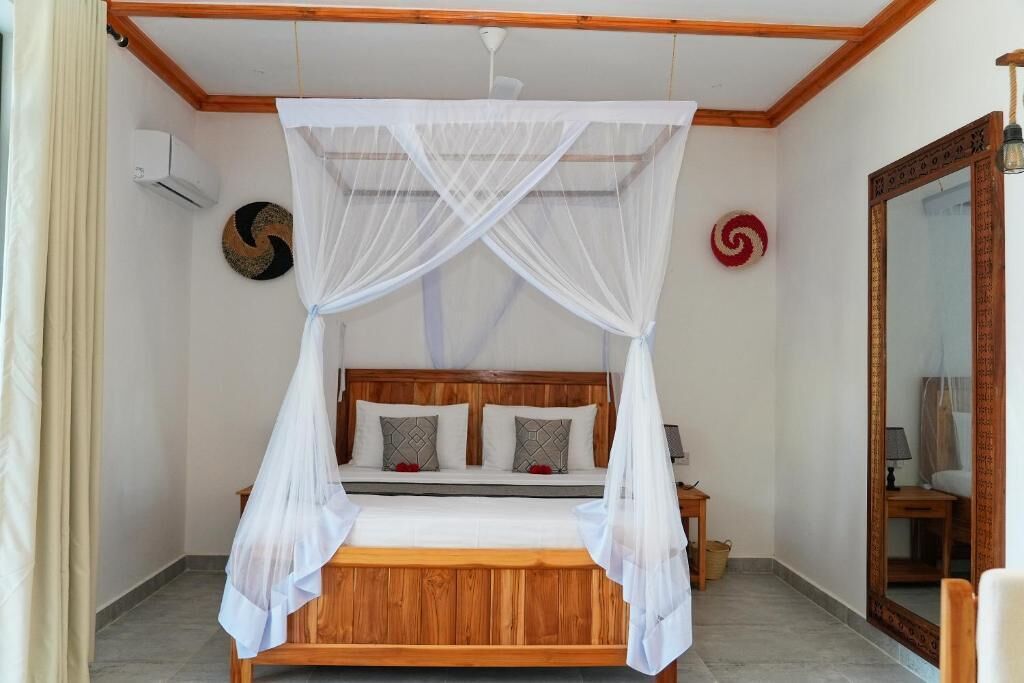 Un dormitorio con una cama de madera, dosel blanco y un espejo en la pared.