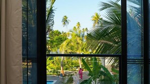 Blick durch ein Fenster auf einen Poolbereich, umgeben von Palmen und viel Grün.