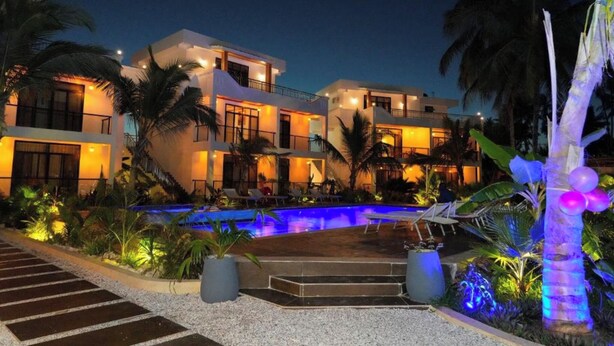 Ein modernes Hotel mit Schwimmbad, Palmen und einer gut beleuchteten Fassade.