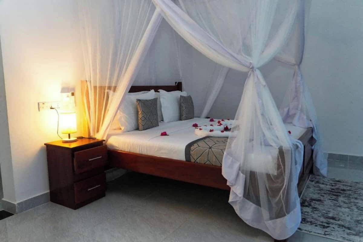 A bed with a canopy, a bedside table with a lamp, and a patterned rug.