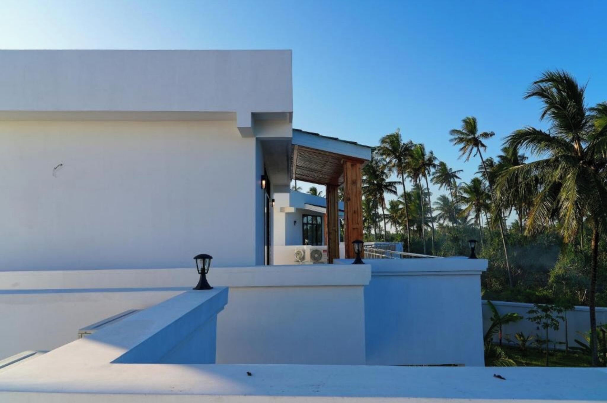A modern building with a flat roof, a covered outdoor area, and a view of palm trees.