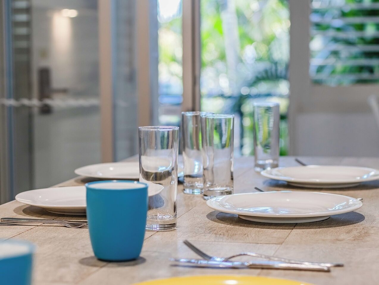A dining table set with plates, glasses, and cutlery, with a blue cup in the foreground.