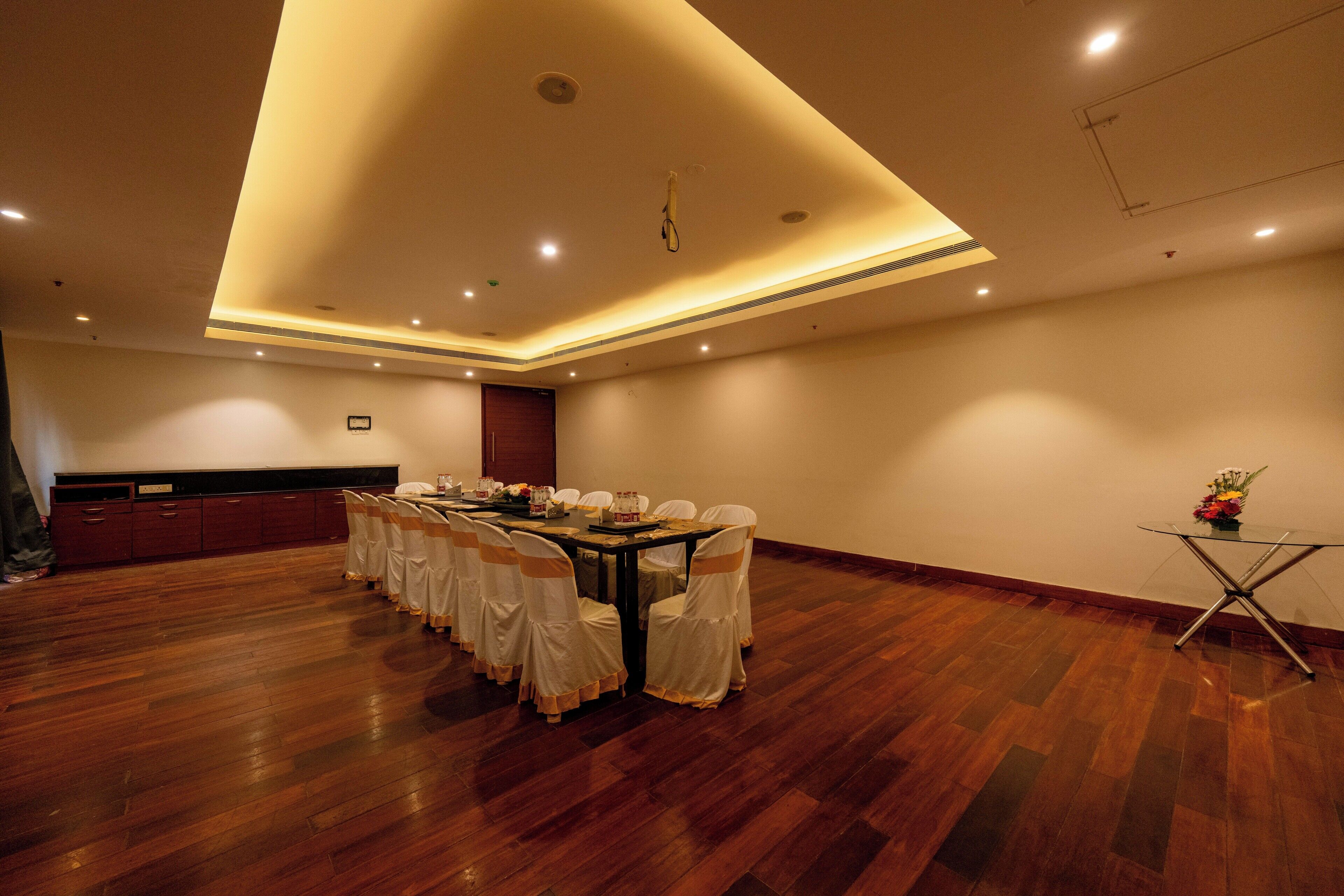 A conference room with a round table, chairs, and a small side table with a vase.