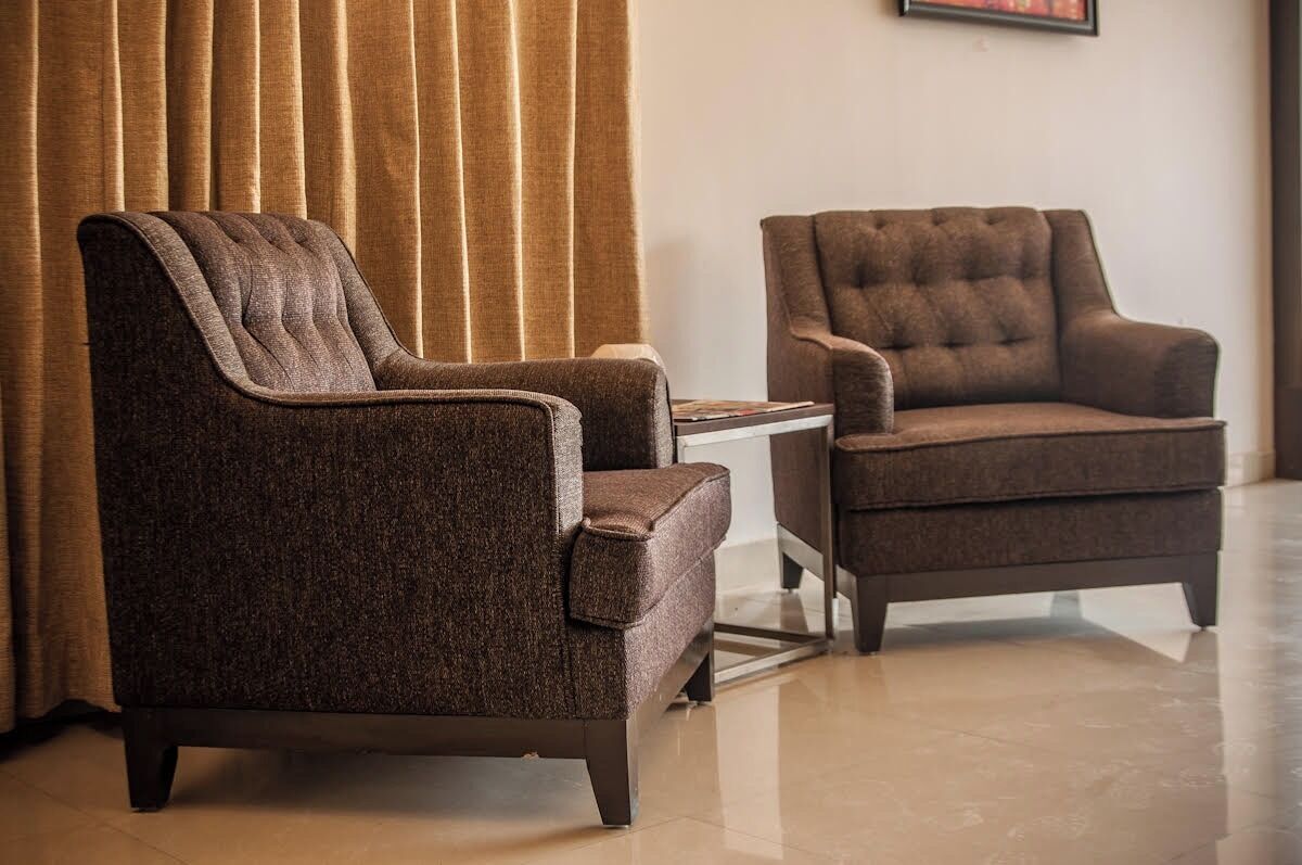 Dos sillones con diseño capitonado, una mesita y una cortina en una habitación con suelo de baldosas.