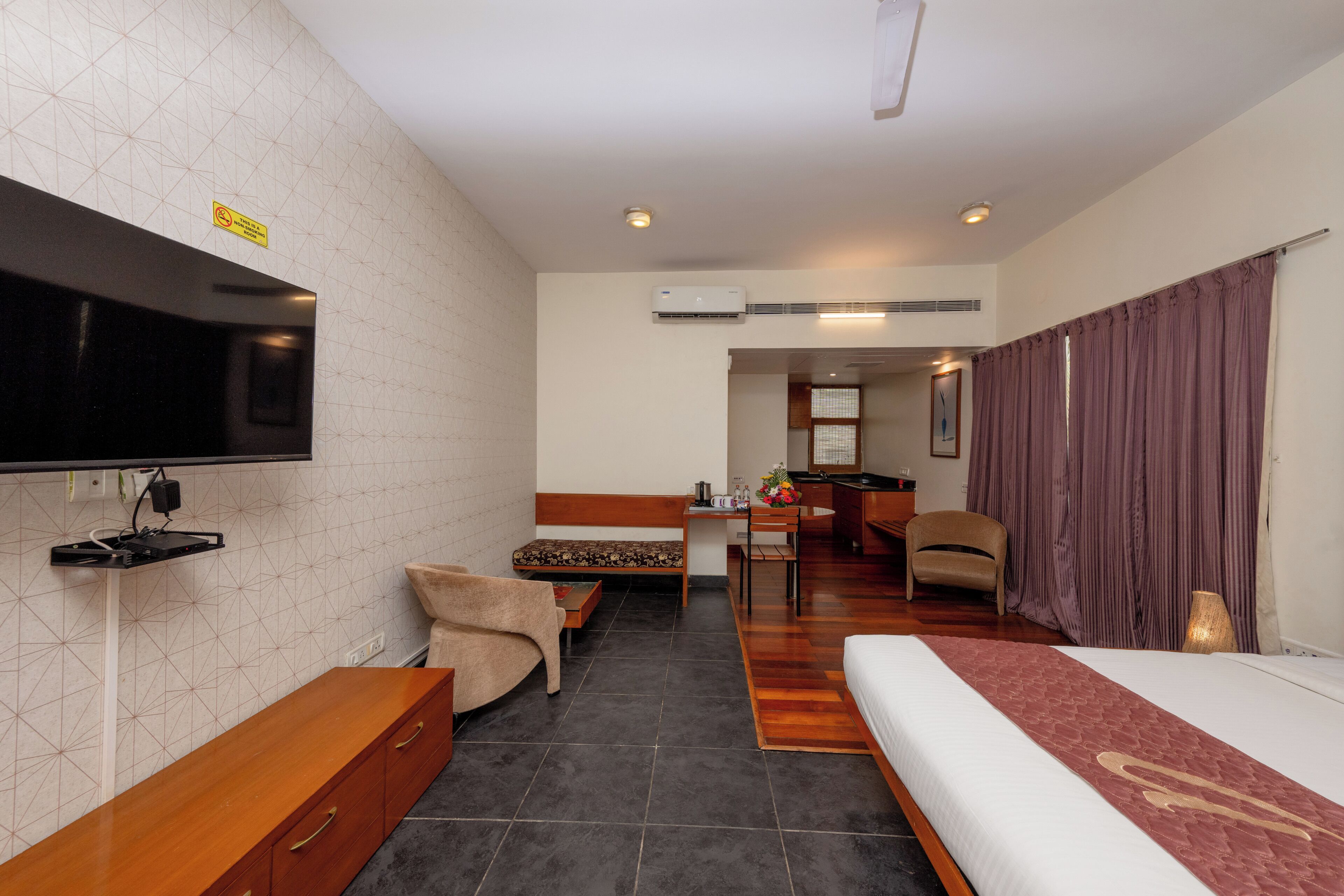 A hotel room with a bed, a desk, a chair, a TV, and an air conditioning unit.