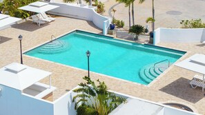 Ein rechteckiger Pool mit Fliesen umgeben, mit Liegestühlen und Blumentöpfen.