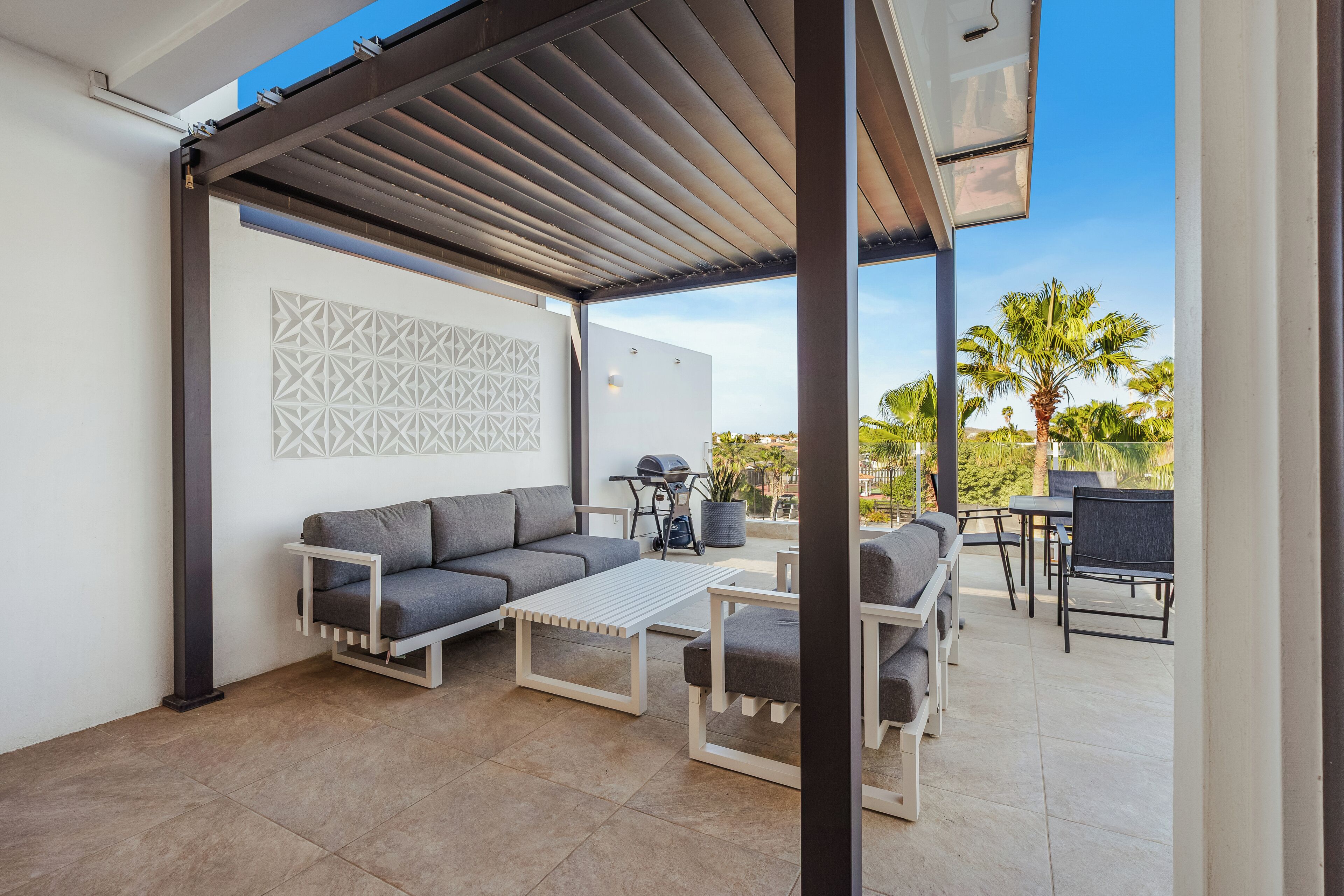 Une terrasse extérieure aménagée avec un canapé, une table, des chaises et un barbecue.
