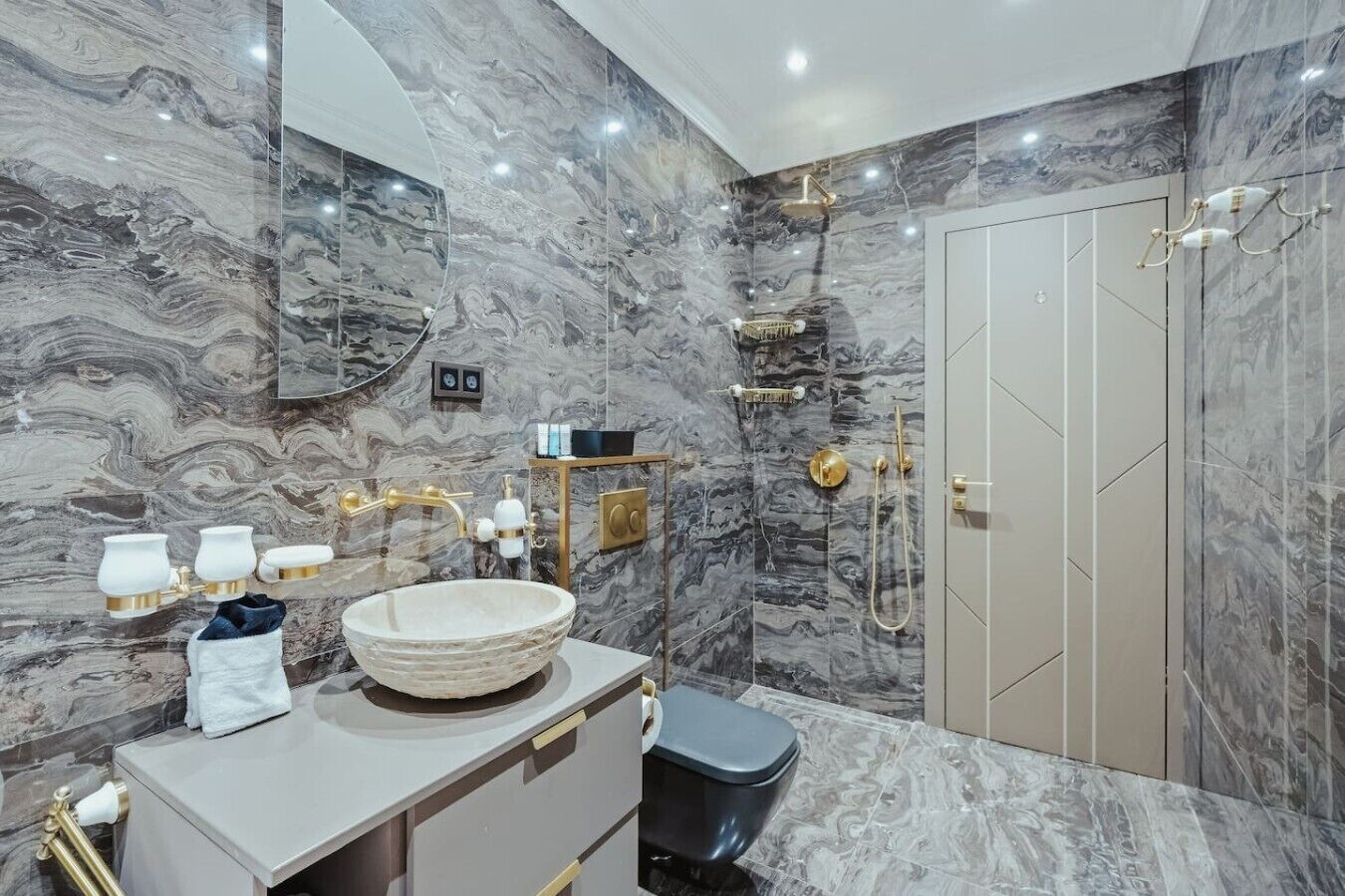 A bathroom with a marble wall, a round sink, a toilet, and a shower area.