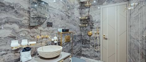 A bathroom with a marble wall, a round sink, a toilet, and a shower area.