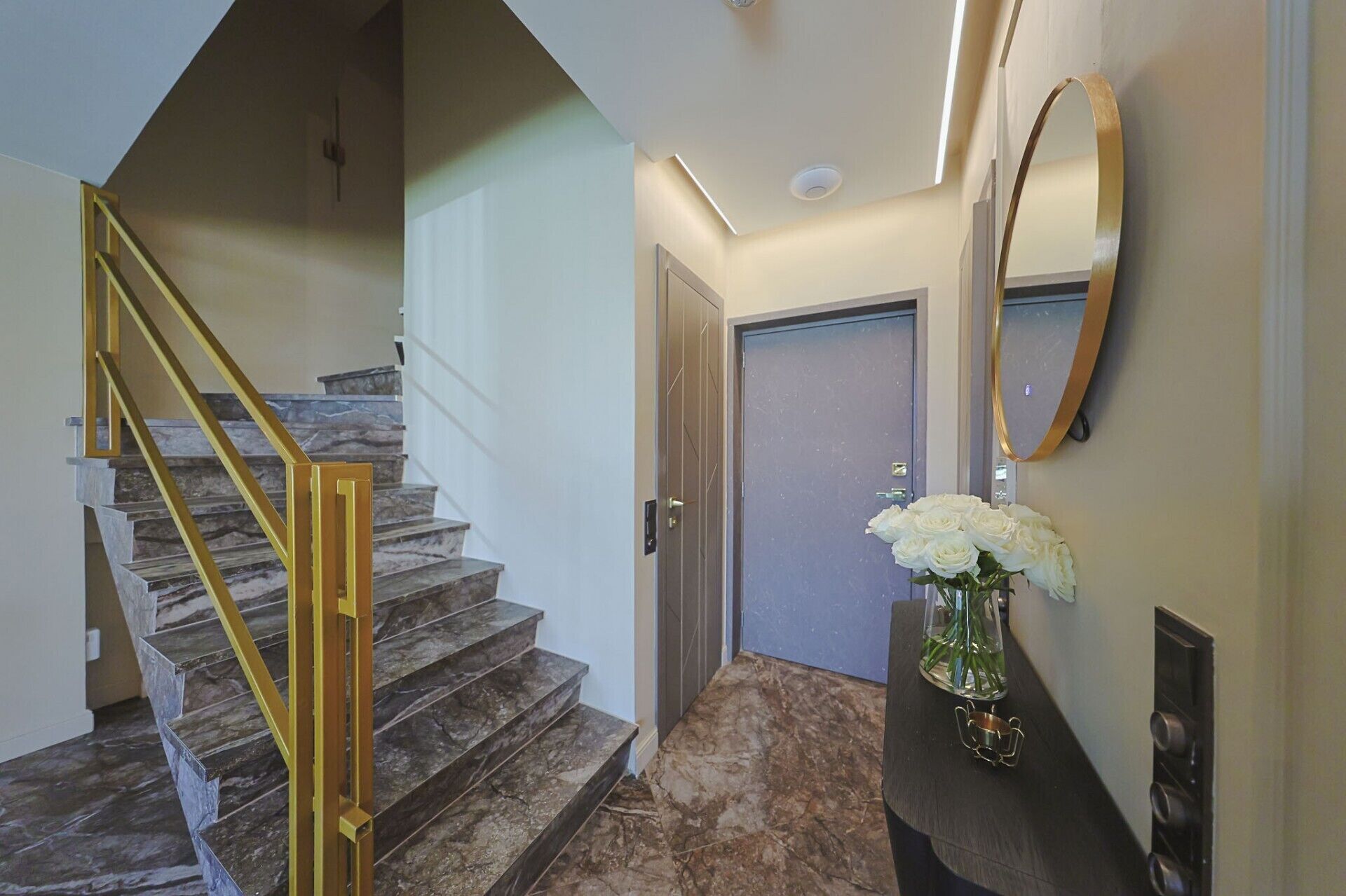 A staircase with marble steps and a golden handrail, leading to a door with a mirror above it.