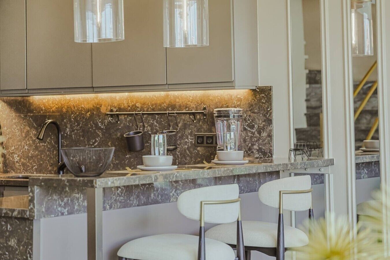 Una cocina moderna con encimera de mármol, licuadora integrada, utensilios colgantes y un taburete de bar.