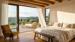 Een slaapkamer met een groot bed, een stoel, een bankje en uitzicht op de omgeving.