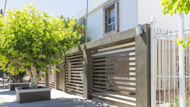 A gated residential area with a tree, a white fence, and a building with a window. - Casa Rebeca3 Complete, ideal for large groups, work teams, vacations, etc. (Chihuahua)