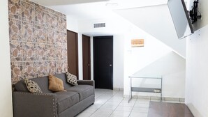A living room with a stone wall, a sofa with patterned cushions, a wooden coffee table, and a TV mounted on the wall. - Casa Rebeca3 Complete, ideal for large groups, work teams, vacations, etc. (Chihuahua)